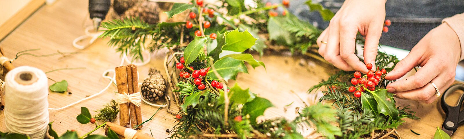 Two hands construct a holiday wreath on a wooden table Two hands construct a holiday wreath on a wooden table